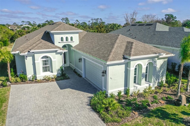 mediterranean / spanish home with a shingled roof, decorative driveway, an attached garage, and stucco siding