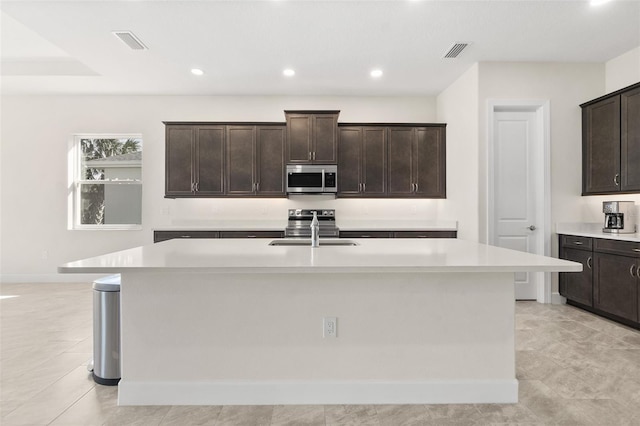 kitchen with a sink, stainless steel appliances, an island with sink, and light countertops