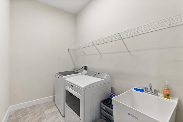 washroom featuring a sink, laundry area, washing machine and dryer, and baseboards