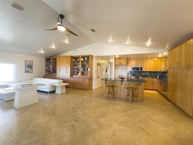 kitchen with dark countertops, visible vents, stainless steel microwave, lofted ceiling, and a large island with sink