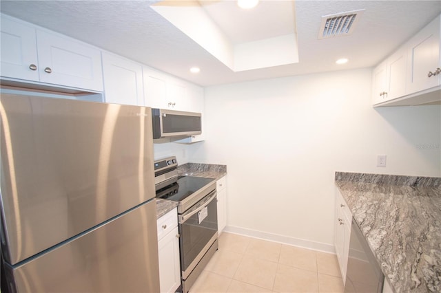 kitchen with appliances with stainless steel finishes, a textured ceiling, white cabinets, stone counters, and light tile patterned floors