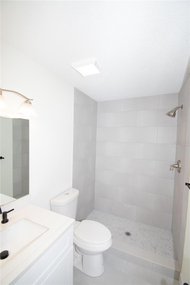 bathroom featuring vanity, a tile shower, and toilet