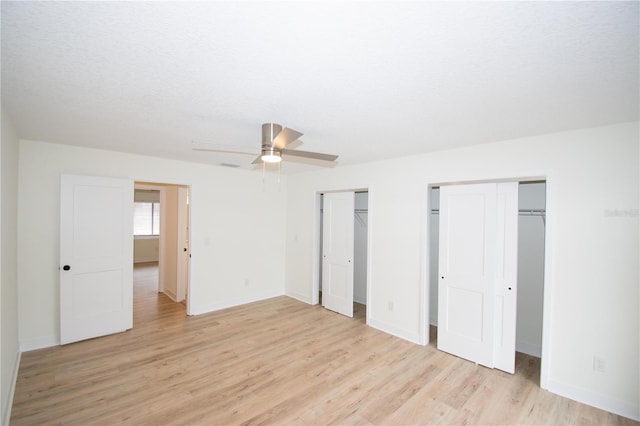 unfurnished bedroom with ceiling fan, multiple closets, a textured ceiling, and light hardwood / wood-style flooring