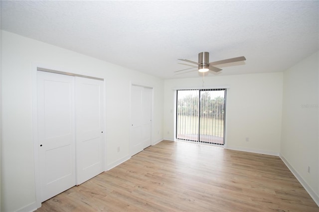 unfurnished bedroom with light hardwood / wood-style flooring, multiple closets, access to outside, a textured ceiling, and ceiling fan