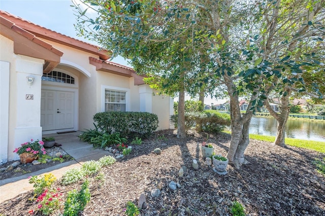 doorway to property featuring a water view, a tile roof, and stucco siding