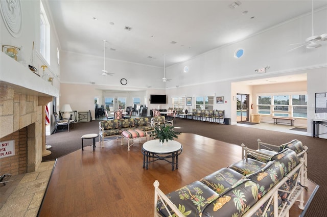 carpeted living room with a ceiling fan, a stone fireplace, and a towering ceiling