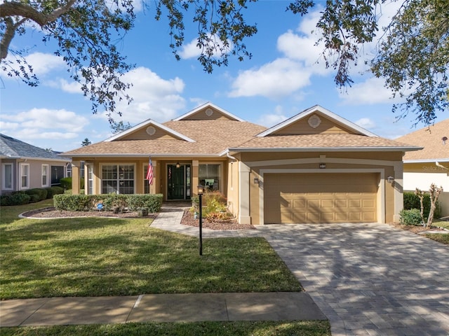 ranch-style house with decorative driveway, stucco siding, a shingled roof, a garage, and a front lawn