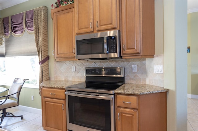 kitchen with stainless steel appliances, brown cabinets, light tile patterned flooring, and light stone countertops