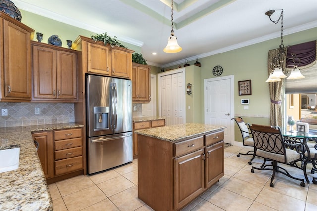 kitchen with stainless steel fridge, light stone counters, brown cabinets, hanging light fixtures, and crown molding