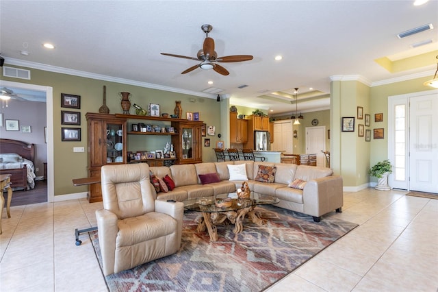 living room with light tile patterned flooring, visible vents, baseboards, a raised ceiling, and crown molding