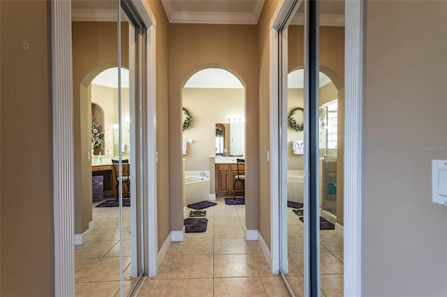 hallway featuring baseboards, ornamental molding, arched walkways, and light tile patterned flooring