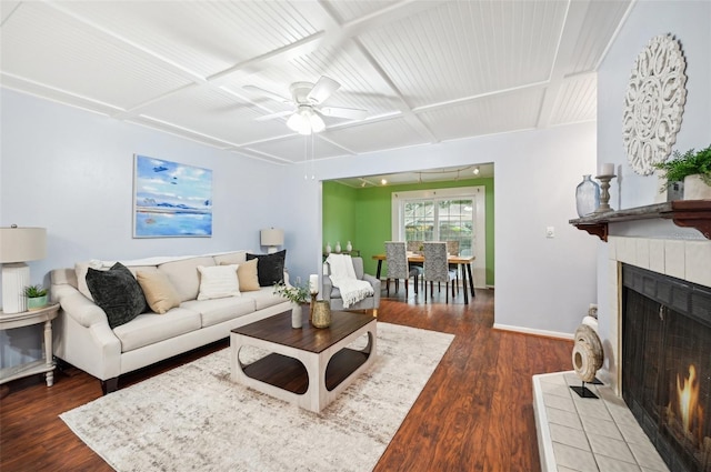 living room with a tile fireplace, coffered ceiling, dark wood-type flooring, and ceiling fan