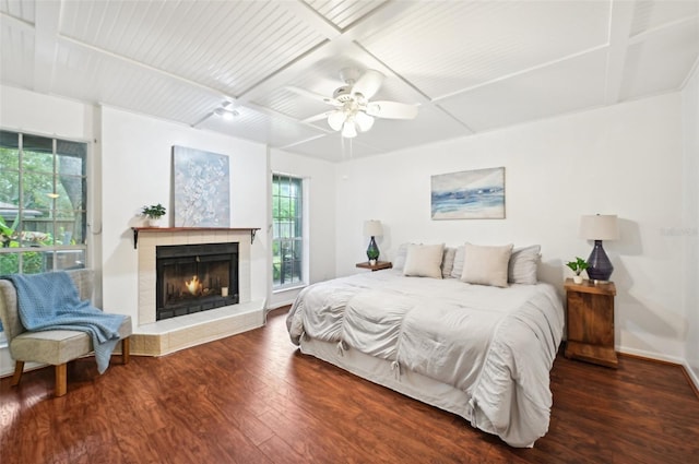 bedroom featuring ceiling fan, a tiled fireplace, and dark hardwood / wood-style flooring