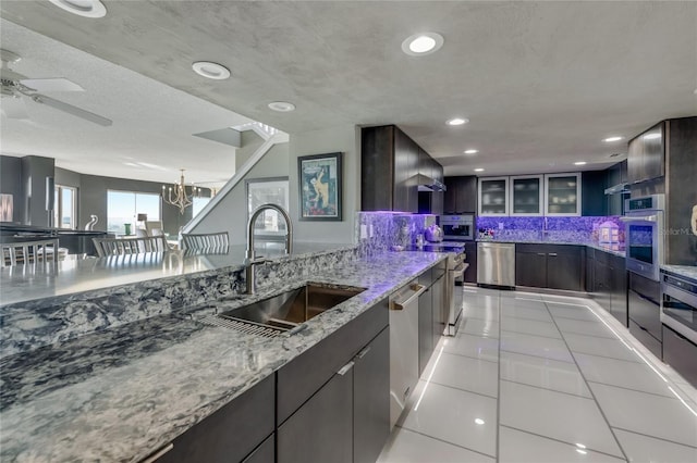 kitchen with light tile patterned floors, a sink, appliances with stainless steel finishes, light stone countertops, and glass insert cabinets