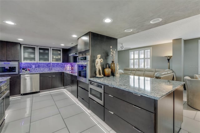 kitchen featuring light stone counters, light tile patterned flooring, stainless steel appliances, modern cabinets, and glass insert cabinets