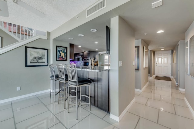 kitchen featuring a breakfast bar area, visible vents, a textured ceiling, light stone countertops, and a peninsula