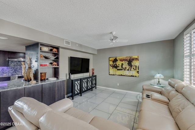 living area featuring a ceiling fan, visible vents, a textured ceiling, and baseboards