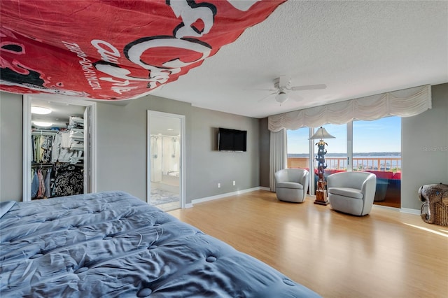 bedroom featuring a ceiling fan, a textured ceiling, ensuite bath, wood finished floors, and baseboards