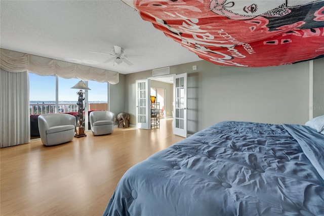 bedroom featuring a textured ceiling, ceiling fan, a city view, wood finished floors, and french doors