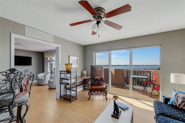 living room with a textured ceiling, light wood-style flooring, visible vents, baseboards, and a ceiling fan