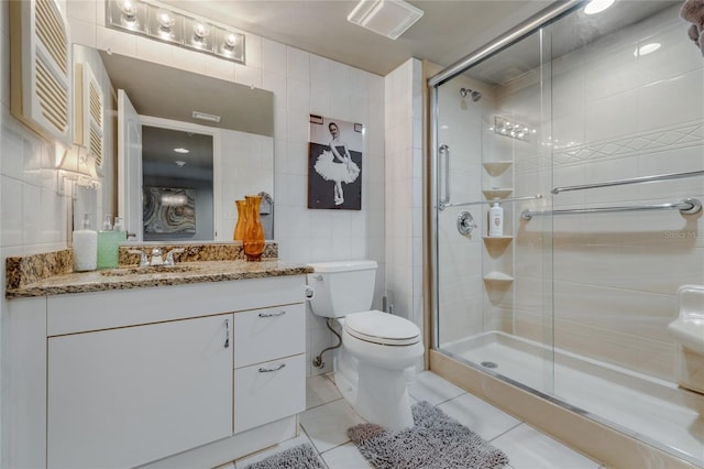 bathroom with a stall shower, toilet, tile patterned flooring, vanity, and tile walls