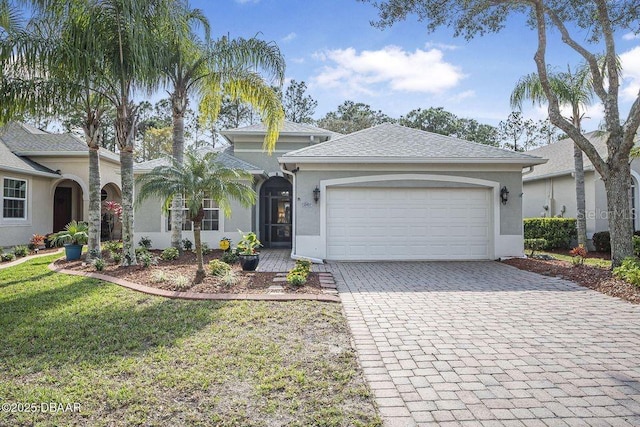 view of front of home with a garage, decorative driveway, a front yard, and stucco siding