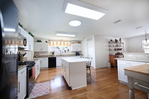 kitchen featuring black appliances, a kitchen island, white cabinetry, and light countertops