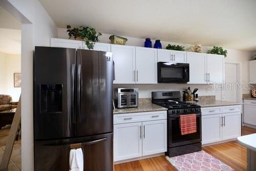 kitchen with white cabinets, gas range, black microwave, and stainless steel refrigerator with ice dispenser