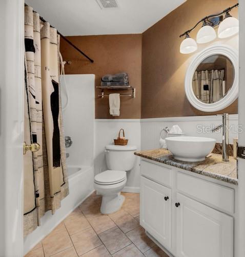 bathroom featuring a wainscoted wall, visible vents, shower / bathtub combination with curtain, vanity, and tile patterned floors