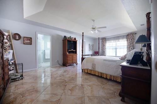 bedroom featuring marble finish floor, a raised ceiling, a ceiling fan, ensuite bath, and baseboards