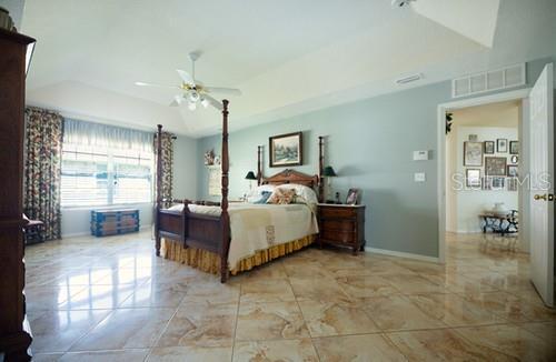 bedroom with a tray ceiling, marble finish floor, visible vents, ceiling fan, and baseboards