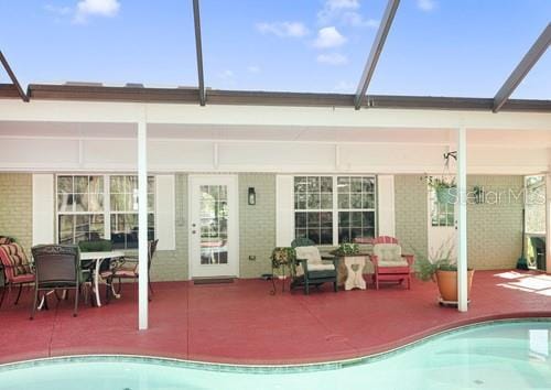 rear view of property with glass enclosure, brick siding, an outdoor pool, and a patio