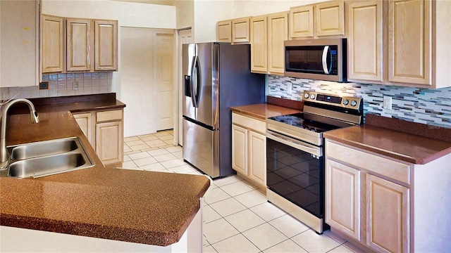 kitchen with light tile patterned floors, dark countertops, appliances with stainless steel finishes, light brown cabinetry, and a sink