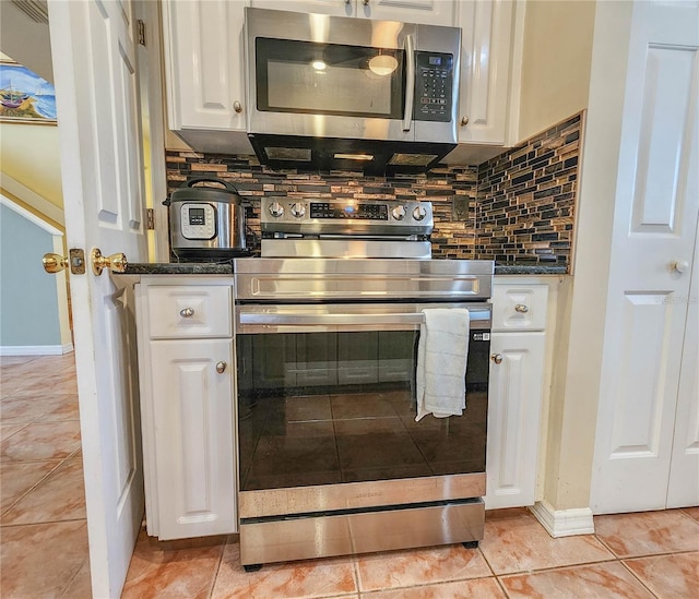 kitchen with light tile patterned floors, dark stone countertops, stainless steel appliances, white cabinetry, and backsplash