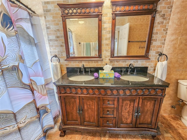 bathroom with toilet, double vanity, and a sink