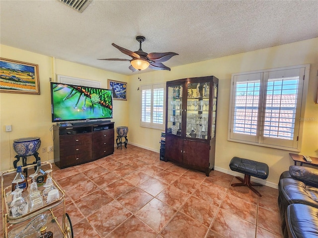 living room with a textured ceiling, visible vents, a ceiling fan, and baseboards