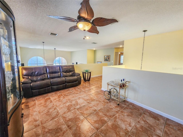 living area with a textured ceiling, ceiling fan, light tile patterned floors, visible vents, and baseboards