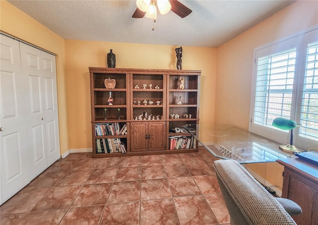 tiled office space featuring a textured ceiling, ceiling fan, and baseboards