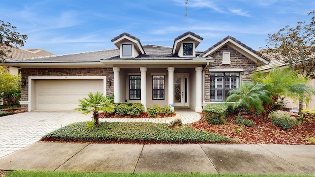 view of front of property with decorative driveway, stone siding, a tiled roof, and a garage