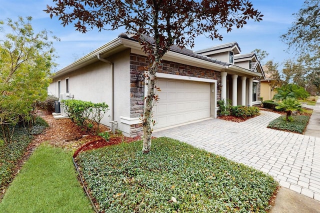 view of side of property featuring a garage, stone siding, decorative driveway, and stucco siding