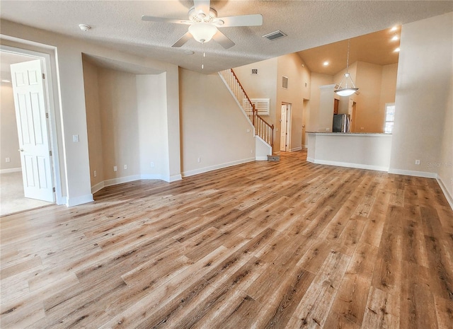 unfurnished living room with visible vents, a ceiling fan, stairs, baseboards, and light wood-type flooring