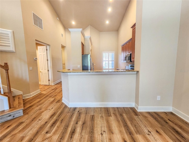 kitchen featuring light wood finished floors, visible vents, appliances with stainless steel finishes, brown cabinetry, and light stone countertops