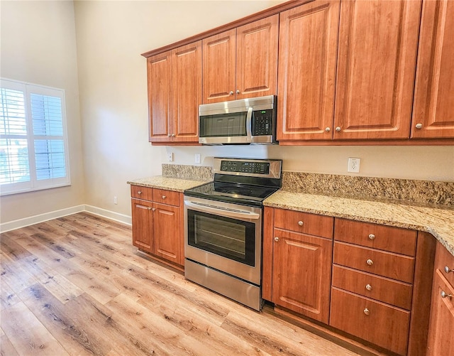 kitchen with stainless steel appliances, brown cabinetry, light wood-type flooring, and light stone countertops