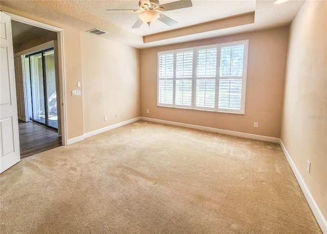 carpeted spare room featuring a textured ceiling, a ceiling fan, visible vents, baseboards, and a raised ceiling