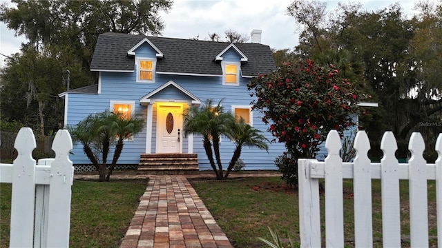 view of front of house with entry steps, a fenced front yard, a chimney, roof with shingles, and a front lawn