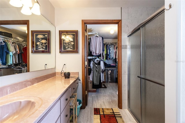 full bathroom featuring wood finished floors, a stall shower, a walk in closet, and vanity