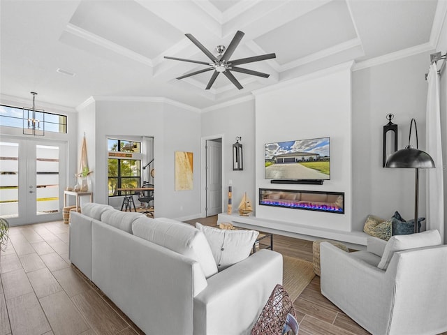 living area with wood finish floors, a high ceiling, ornamental molding, a glass covered fireplace, and coffered ceiling