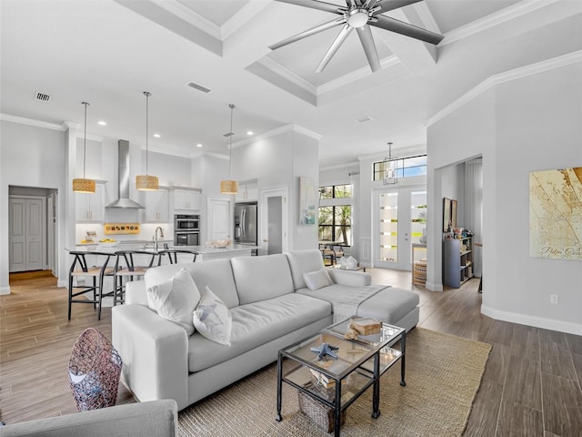 living area with visible vents, coffered ceiling, baseboards, light wood-style flooring, and a high ceiling