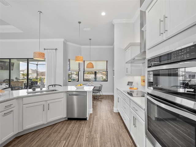 kitchen featuring white cabinets, wall chimney range hood, stainless steel appliances, and decorative light fixtures