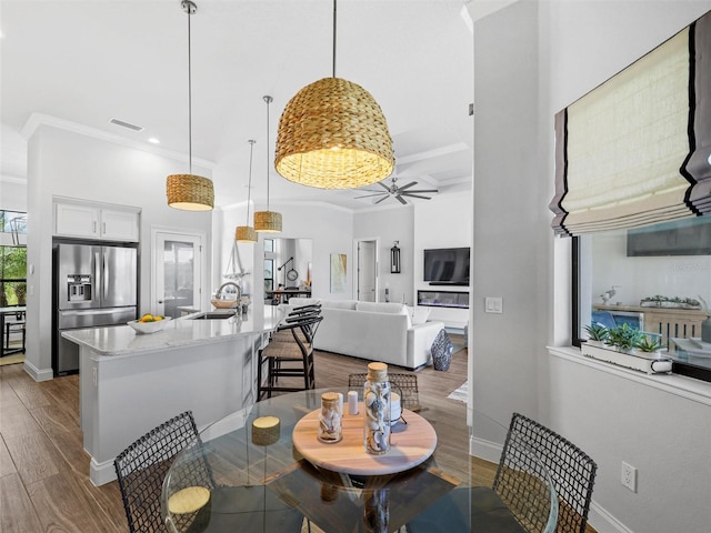 dining room with baseboards, visible vents, a ceiling fan, ornamental molding, and light wood-type flooring